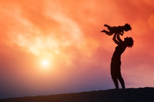 Mother lifting toddler child in air over scenic sunset sky