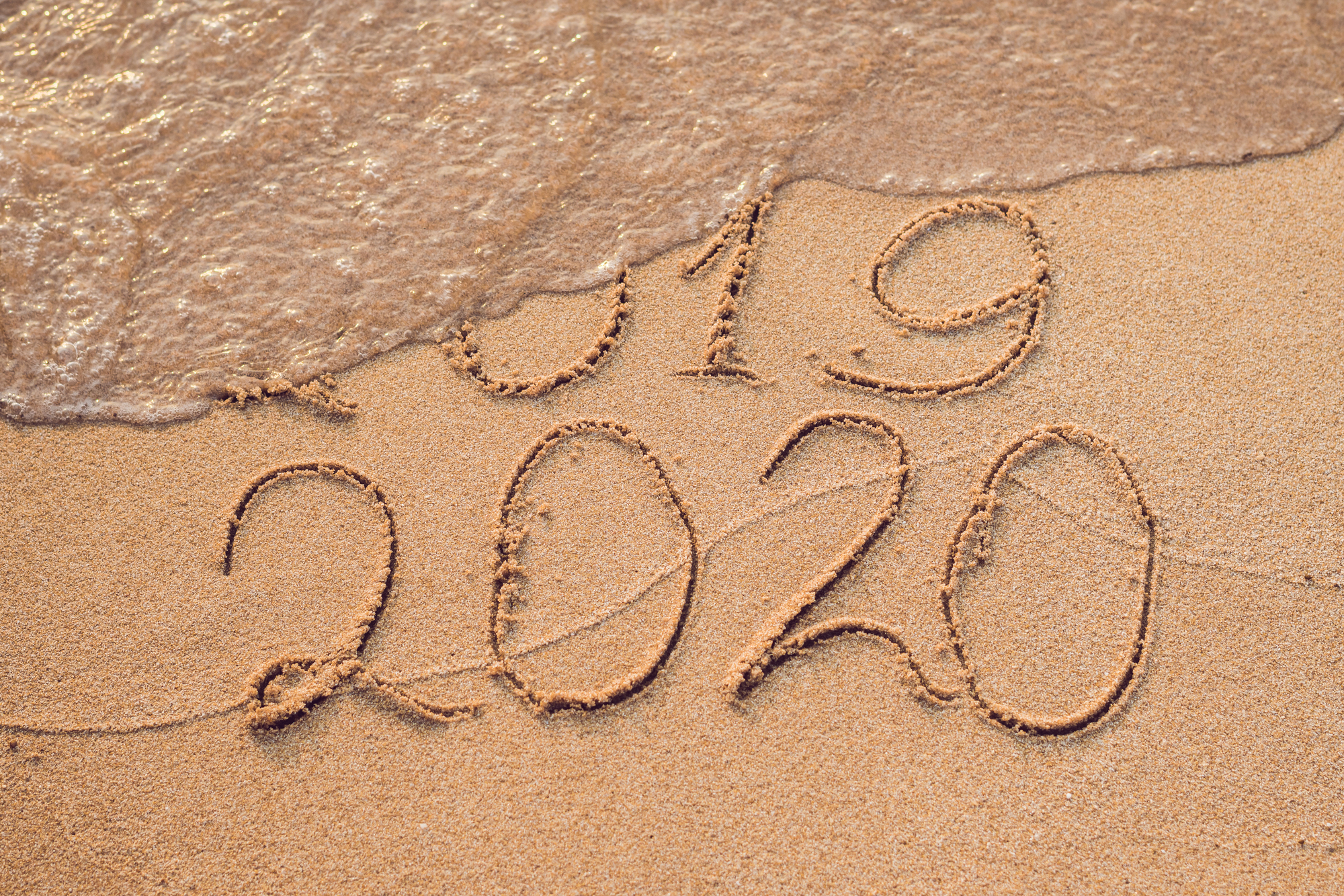 New Year 2020 is coming concept - inscription 2019 and 2020 a beach sand, the wave is almost covering the digits 2019.
